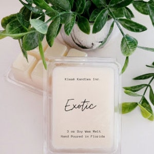May include: A white wax melt cube with the text "Exotic" printed on the front. The wax melt is packaged in a clear plastic container with the text "Klass Candles Inc." and "3 oz Soy Wax Melt Hand Poured in Florida" printed on the label.