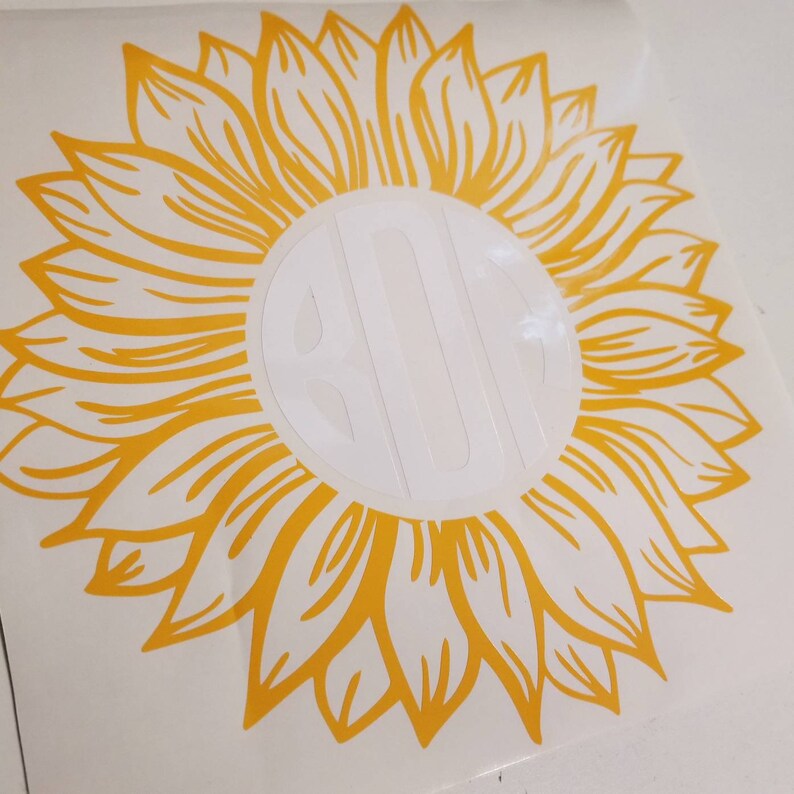 K&ouml;nnte beinhalten: Ein gelber Sonnenblumen-Aufkleber mit einem wei&szlig;en Kreis in der Mitte. Der Kreis enth&auml;lt ein Monogramm.