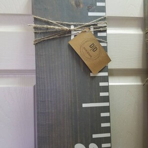 May include: A gray wooden growth chart with white markings and a white number "2" at the bottom. A brown tag with the text "D&D Divine Designs" is tied to the chart with twine.