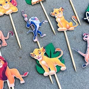 May include: A set of 10 Lion King themed cupcake toppers. The toppers feature Simba, Mufasa, Pumbaa, Timon, and Rafiki. The toppers are printed on cardstock and attached to wooden skewers.