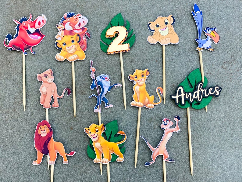 May include: A set of 10 Lion King themed cake toppers. The toppers feature characters from the movie, including Simba, Nala, Timon, Pumbaa, and Zazu. There is also a number 2 topper and a topper that says "Andres".