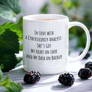 May include: White ceramic coffee mug with black text that reads "In love with a cybersecurity analyst: She's got my heart on lock and my data on backup."