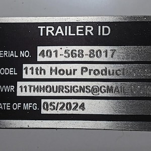 May include: A rectangular metal plate with the text "TRAILER ID". It includes the serial number "401-568-8017", the model "11th Hour Production", GVWR, and the date of manufacture "05/2024". The plate has rounded corners and mounting holes.