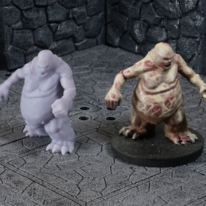 Può includere: Due miniature di creature grottesche. Una è una figura carnosa di colore pallido con una bocca spalancata e una superficie testurizzata. L'altra è una figura carnosa grigia con una bocca spalancata simile e una superficie liscia.