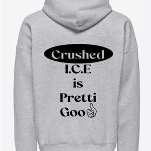 May include: A light gray hoodie with the text "Crushed I.C.E is Pretti Goo" in black. The design includes a thumbs-up graphic. The hoodie has a hood and long sleeves. A yellow banner in the top left corner reads "Almost sold out."