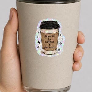 May include: A holographic sticker on a beige travel mug featuring a coffee cup illustration with a brown sleeve. The text on the sleeve reads, "powered by caffeine & plot twists," surrounded by small black star icons on a shimmering iridescent background.