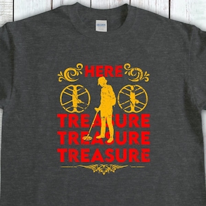 May include: Dark gray t-shirt with a yellow and red graphic. The graphic features a silhouette of a person using a metal detector, the word "TREASURE" in red, and the word "HERE" in yellow.