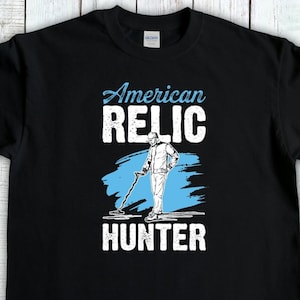 May include: Black t-shirt with the words "American Relic Hunter" in white and light blue. The design features a person using a metal detector. The shirt is made of a soft material and is suitable for casual wear.