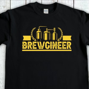 May include: Black t-shirt featuring a yellow graphic of a brewery with the text "BREWGINNEER" in a vintage style font.
