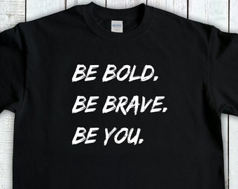Op de afbeelding: Zwart T-shirt met witte tekst die "BE BOLD. BE BRAVE. BE YOU." luidt.
