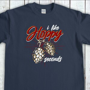 May include: A navy blue t-shirt featuring the phrase "I like Hoppy seconds" in a script font, with two illustrated hops. The text is red and white, with the hops in white and gold.