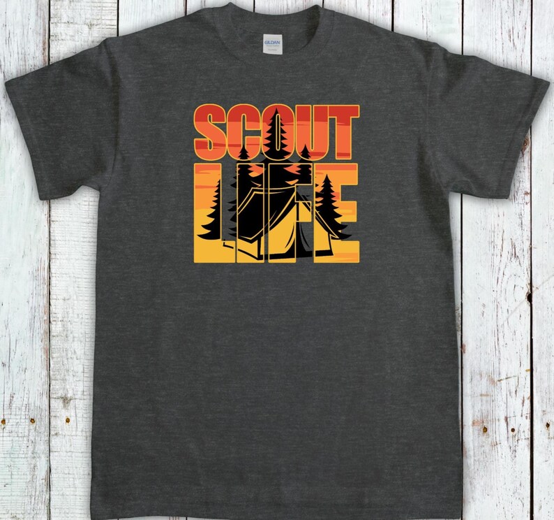 May include: Dark gray t-shirt with the words "SCOUT LIFE" in orange and yellow block letters. The design includes a black tent and trees, set against a sunset background. A Gildan tag is visible.