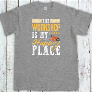 Peut inclure: T-shirt gris avec le texte "The Workshop is my Happy Place" en jaune avec un graphique de tron&ccedil;onneuse.