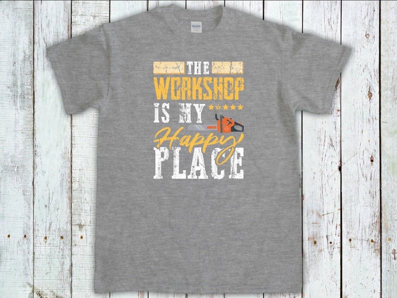 Peut inclure: T-shirt gris avec le texte "The Workshop is my Happy Place" en jaune avec un graphique de tron&ccedil;onneuse.