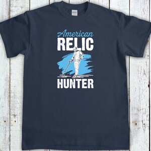 May include: Navy blue t-shirt with the words "American Relic Hunter" in white and light blue. The design features a graphic of a person using a metal detector. A great gift for treasure hunters.