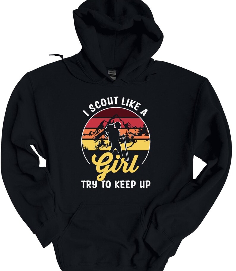 May include: Black hooded sweatshirt with a graphic design. The design features a hiker silhouette within a circular sunset scene, with the text "I SCOUT LIKE A Girl TRY TO KEEP UP" in white and yellow.