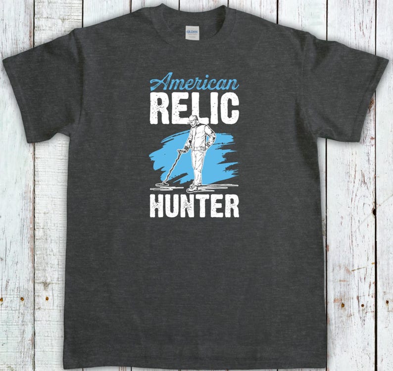 May include: Dark gray t-shirt with the words "American Relic Hunter" in white and light blue. The design features a person using a metal detector. The shirt is made of a soft, comfortable material.
