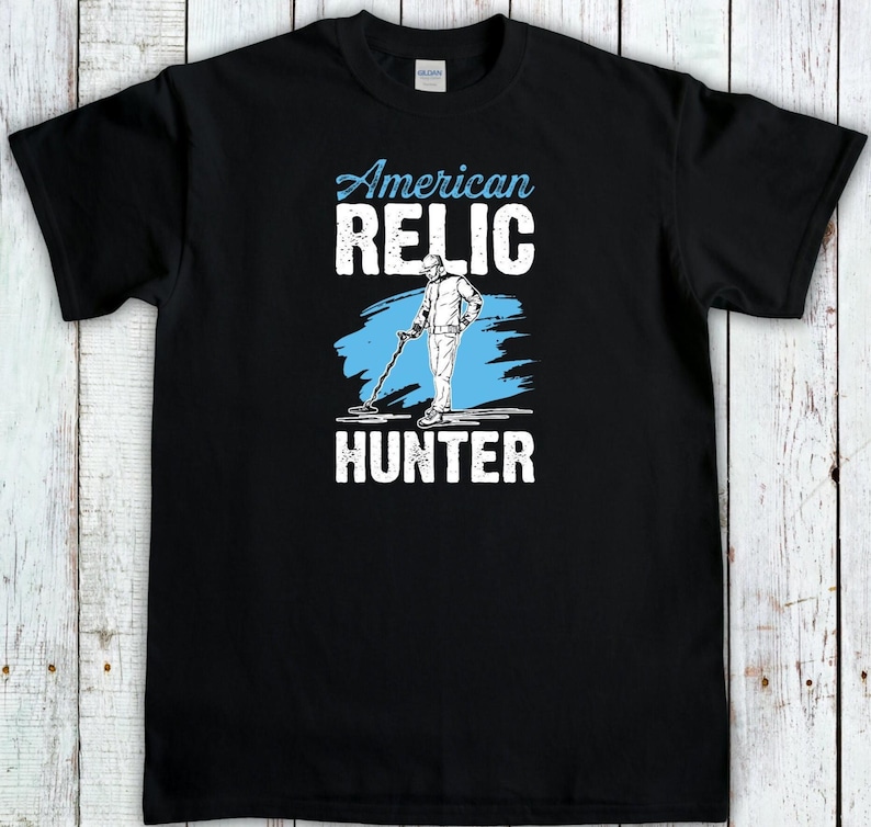 May include: Black t-shirt with the words "American Relic Hunter" in white and light blue. The design features a person using a metal detector. The shirt is made of a soft material and is suitable for casual wear.