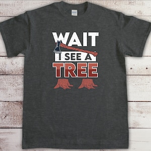 May include: A dark gray t-shirt with a white graphic that says "WAIT I SEE A TREE" with an axe and tree stumps.