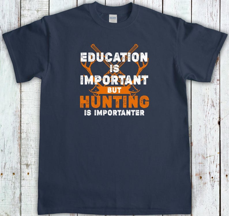 May include: Navy blue t-shirt with the text "EDUCATION IS IMPORTANT BUT HUNTING IS IMPORANTER" in white and orange. The design includes two crossed axes. The shirt is made of a soft material.