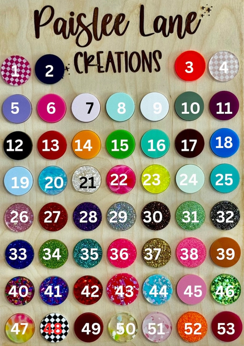May include: A wooden board with 53 numbered, round, colorful, decorative phone grips. The board has the text "Paislee Lane Creations" at the top.
