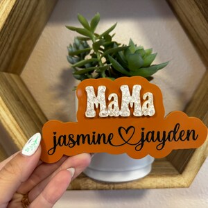 May include: Orange and white wooden sign with the text "Mama jasmine &hearts; jayden" in black lettering.