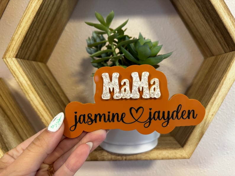 May include: Orange and white wooden sign with the text "Mama jasmine &hearts; jayden" in black lettering.