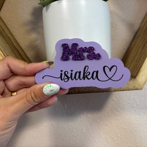 May include: Purple cloud-shaped wooden sign with the text "Mrs. isiaka" in black cursive lettering and a heart symbol. The word "Mrs." is in purple glitter.