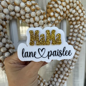 May include: White sign with the word "Mama" in gold glitter letters and the text "lane ♡ paislee" in black cursive.