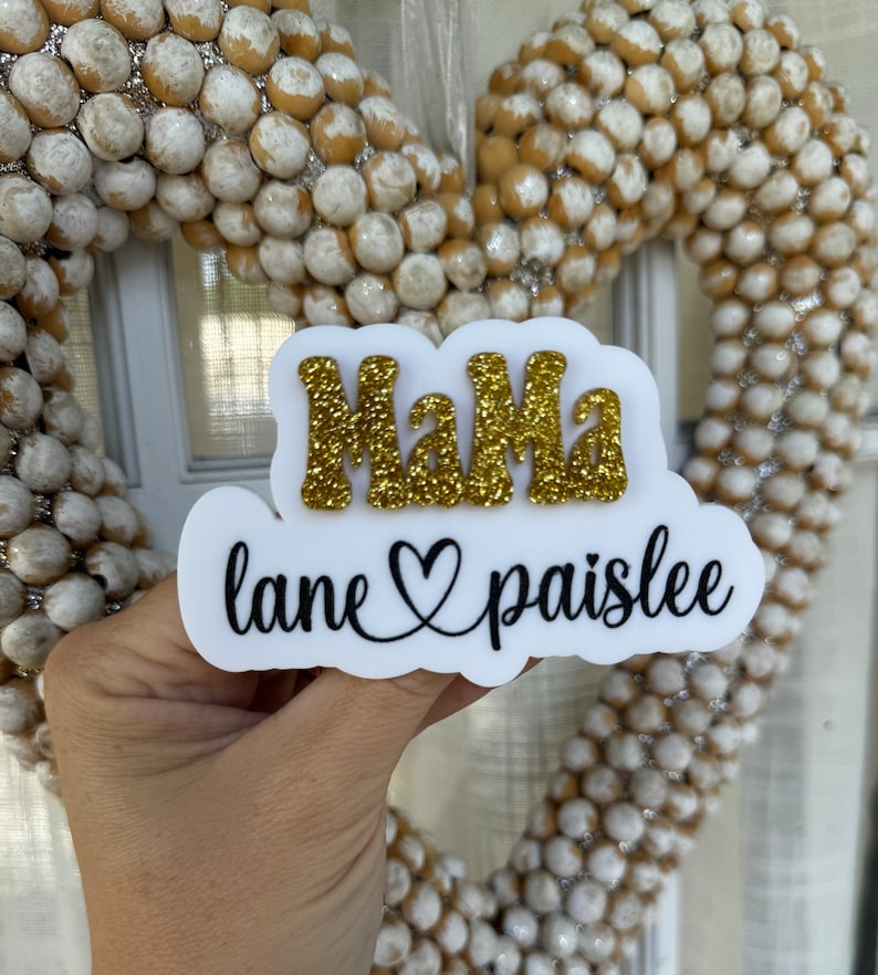 May include: White sign with the word "Mama" in gold glitter letters and the text "lane ♡ paislee" in black cursive.