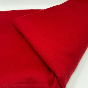 May include: A solid, vibrant red fabric with a soft, matte texture. The material is folded over itself, creating a diagonal crease that highlights the consistent, deep crimson color and the smooth, uniform surface of the textile throughout.