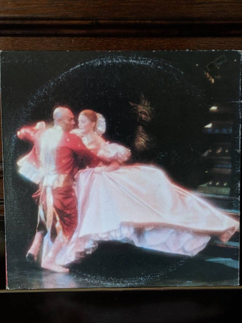 May include: A black and white photograph of a couple dancing. The woman is wearing a white dress and the man is wearing a red jacket. The couple are dancing in a ballroom setting.