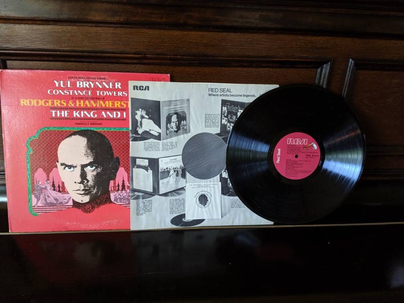 May include: A red vinyl record album cover featuring a black and white photo of Yul Brynner, Constance Towers, and the title "The King and I" by Rodgers & Hammerstein. The album is on the RCA Red Seal label.
