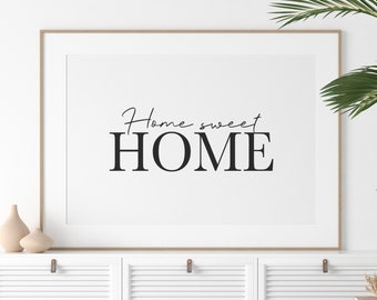 May include: A framed print with the text "Home sweet HOME" in black lettering on a white background. The print is hanging on a white wall above a white cabinet with a wooden top.