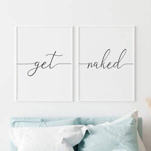 Puede incluir: Dos impresiones enmarcadas blancas con caligraf&iacute;a negra sobre fondo blanco. Las impresiones est&aacute;n colgadas sobre una cama con un edred&oacute;n y almohadas de color azul claro. El texto en las impresiones dice "get" y "naked".