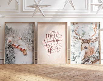 May include: Three framed prints with a winter theme. The left print shows a snowy forest with a red train traveling through it. The middle print has a red inscription that reads "It's the most wonderful time of the year." The right print shows a deer in a snowy forest.
