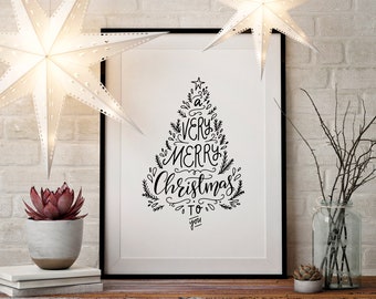 May include: A black and white printable art print with a Christmas tree design and the text "A Very Merry Christmas to You". The print is framed and displayed on a white brick wall with two white paper star lanterns hanging above.