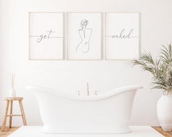 May include: Three framed prints in a bathroom setting. The prints are hung on a white wall above a white bathtub. The left print says "get" in cursive. The middle print is a line drawing of a woman's back. The right print says "naked" in cursive.
