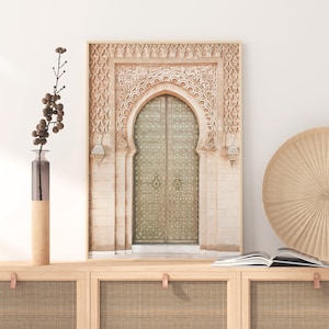 May include: A photograph of a decorative archway with an ornate door. The archway is made of stone and has intricate carvings. The door is made of wood and has a metal design. The photograph is in a light brown frame.