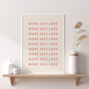 Pu&ograve; includere: Una stampa incorniciata bianca con il testo "MORE SELF LOVE" ripetuto nove volte in rosa chiaro. La stampa &egrave; su uno scaffale di legno con un vaso bianco e due oggetti decorativi in ceramica bianca.