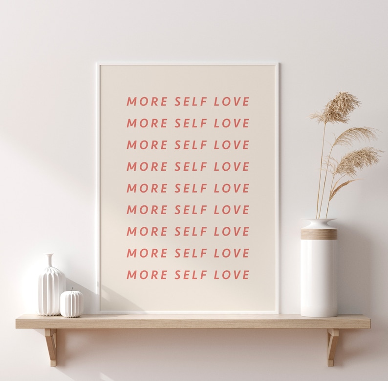 Pu&ograve; includere: Una stampa incorniciata bianca con il testo "MORE SELF LOVE" ripetuto nove volte in rosa chiaro. La stampa &egrave; su uno scaffale di legno con un vaso bianco e due oggetti decorativi in ceramica bianca.