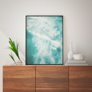 May include: A framed photograph of a turquoise ocean with white waves crashing. A single person is seen surfing in the distance.