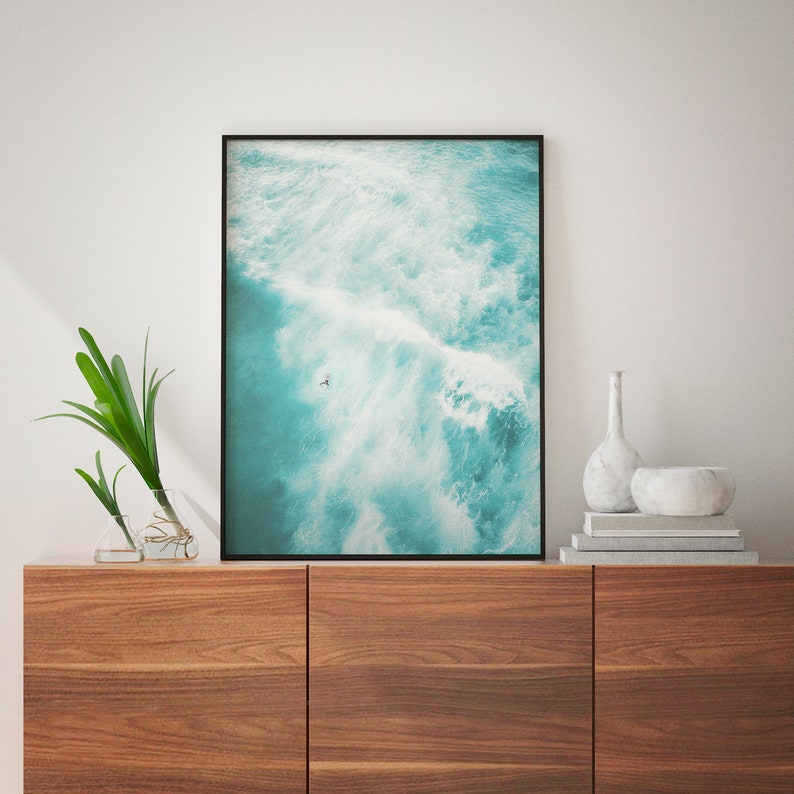 May include: A framed photograph of a turquoise ocean with white waves crashing. A single person is seen surfing in the distance.