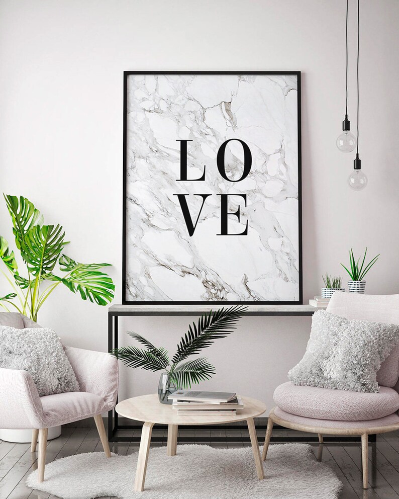 May include: A black framed print with a white marble background and the word "LOVE" in black text. The print is hanging on a white wall above a black console table with two pink chairs and a round wooden coffee table.