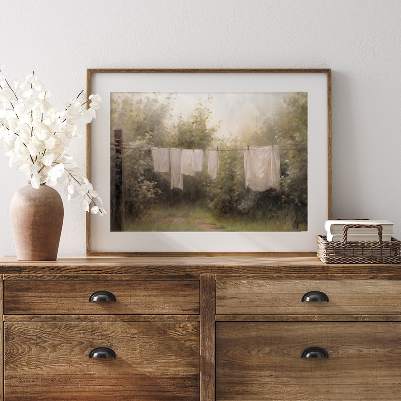 May include: A framed painting of white clothing hanging on a clothesline in a lush green forest setting. The painting has a soft, dreamy feel and evokes a sense of peace and tranquility.