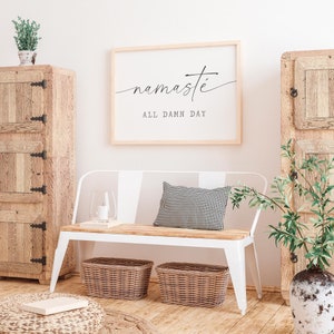 K&ouml;nnte beinhalten: Eine wei&szlig;e Bank mit einem schwarz-wei&szlig; karierten Kissen, zwei Weidenk&ouml;rben und einem gerahmten Druck mit dem Text "namaste all damn day".