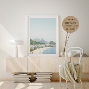 May include: A framed photograph of a beach scene with white buildings and a mountain range in the background. The beach is sandy and the water is blue. The frame is white and the photo is printed on matte paper. The text "50% OFF INSTANT DOWNLOAD 20+ SIZES" is in a brown circle in the upper right corner of the image.