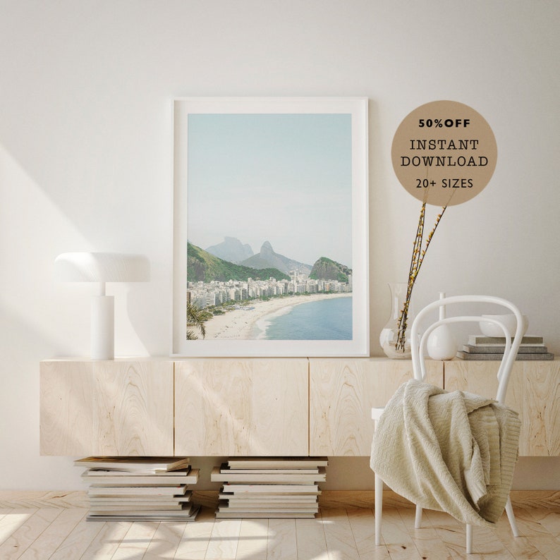 May include: A framed photograph of a beach scene with white buildings and a mountain range in the background. The beach is sandy and the water is blue. The frame is white and the photo is printed on matte paper. The text "50% OFF INSTANT DOWNLOAD 20+ SIZES" is in a brown circle in the upper right corner of the image.