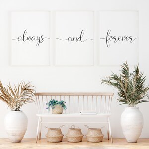 May include: Three framed prints with the words "always", "and", and "forever" in a cursive font. The prints are hanging on a white wall above a white bench with a potted plant and three woven baskets.