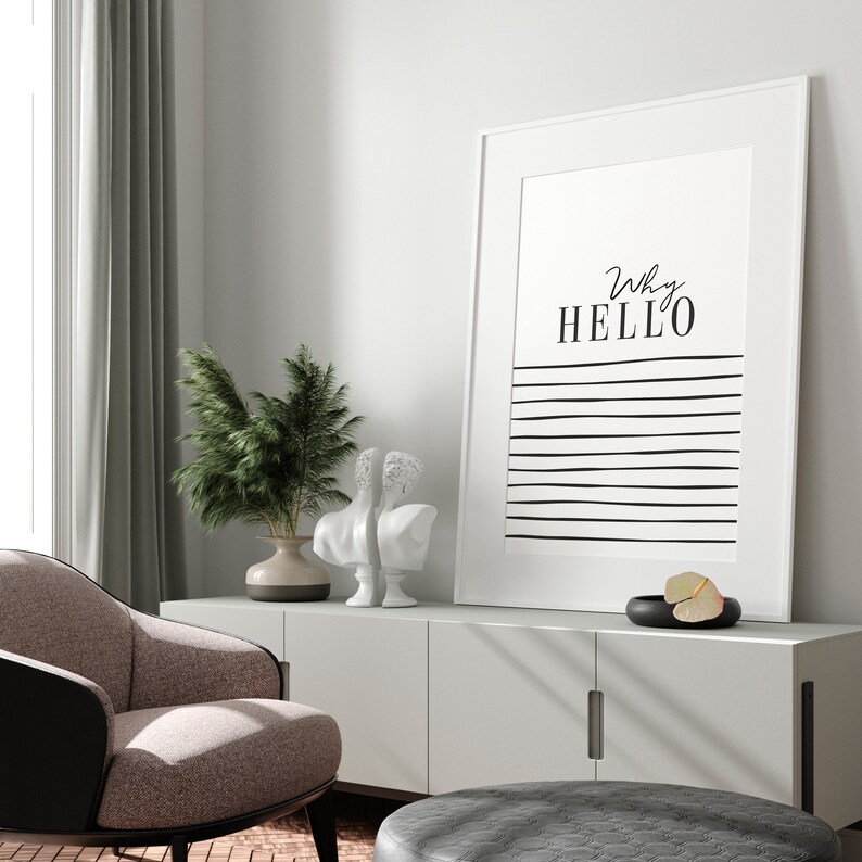 May include: A white framed print with black text that reads "Why HELLO" and black horizontal lines on a white background. The print is hanging on a white wall above a white cabinet with two doors. There are two white statues and a green plant in a brown vase on the cabinet.